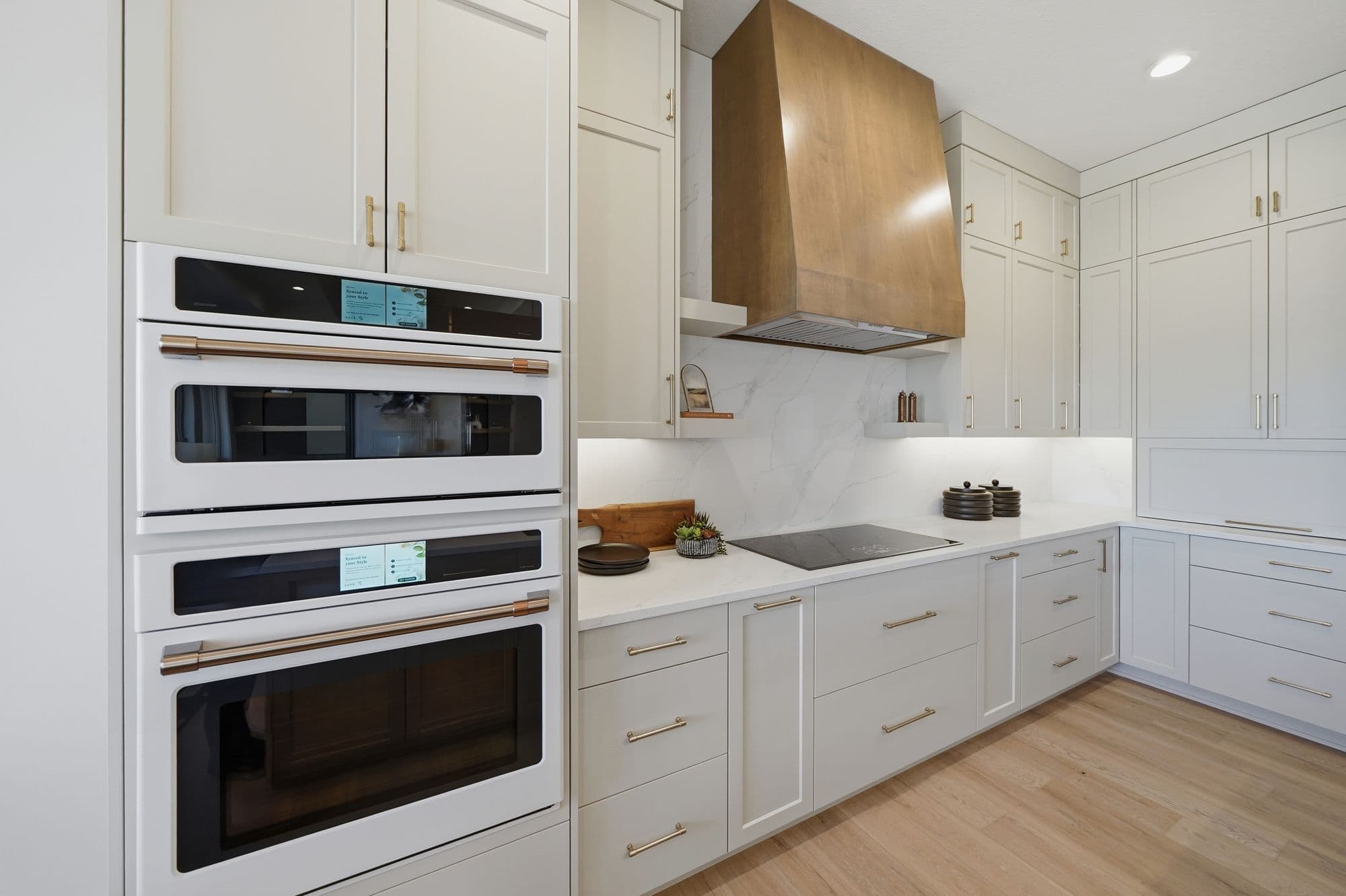 Modern kitchen featuring white cabinets, gold hardware, and stainless steel appliances. A wood range hood is also visible above the stove top.